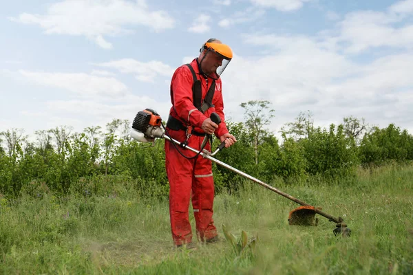 Worker cutting grass with string trimmer outdoors