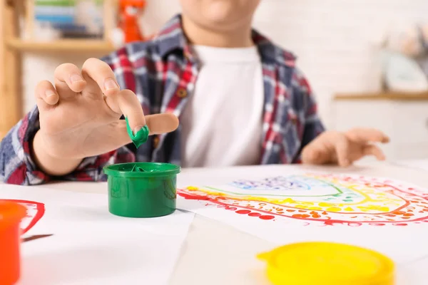 Little boy painting with finger at white table indoors, closeup