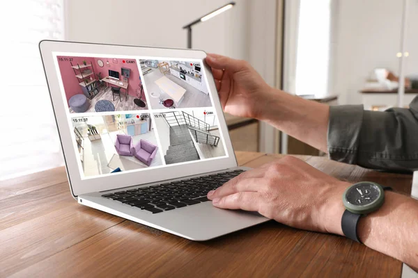 Man monitoring modern CCTV cameras at wooden table, closeup. Smart home security system