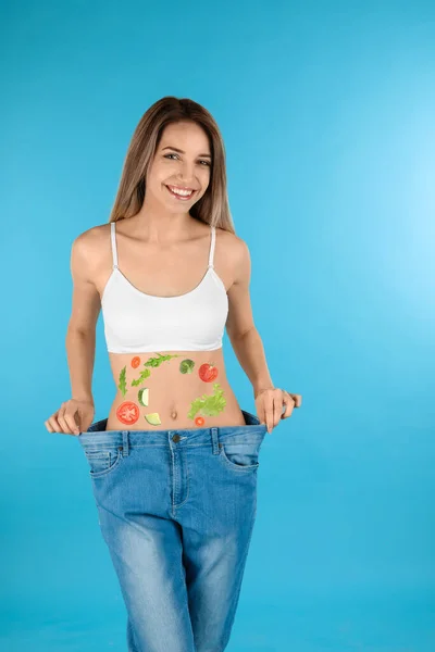 特大のジーンズのスリム女性とターコイズを背景に彼女の腹に野菜のイメージ 健康的な食事 — ストック写真