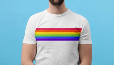 Turkuaz arka planda LGBT gurur bayrağı resmi olan beyaz tişört giyen genç adam, yakın plan.