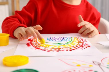 Küçük çocuk beyaz masada parmaklarıyla resim yapıyor, yakın plan.