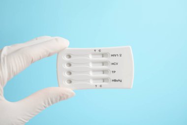 Doctor holding disposable express test for hepatitis on light blue background, closeup