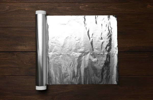 Roll of foil paper on wooden table, top view