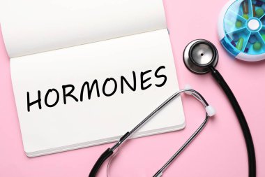 Sözcük hormonları, steteskop ve pembe arka planda haplar içeren defter, düz konum