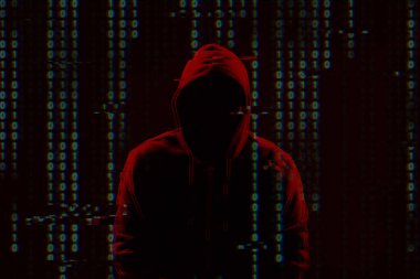 İsimsiz hacker silueti ve karanlık arka planda dijital ikili kod. Siber saldırı kavramı