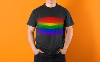 Turuncu arka planda LGBT gurur bayrağı resmi olan siyah tişört giyen genç adam.