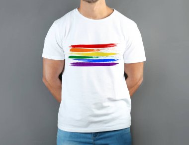 Gri arkaplanda LGBT gurur bayrağı resmi olan beyaz tişört giyen genç adam