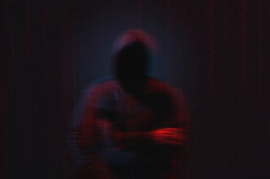 İsimsiz hacker silueti ve karanlık arka planda dijital ikili kod. Siber saldırı kavramı
