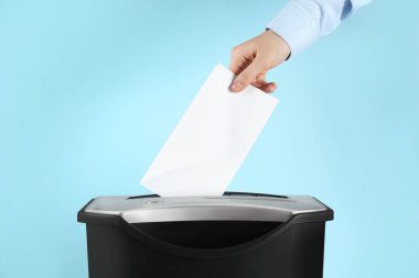 Açık mavi arkaplanda kağıt öğütücüyle zarfı yok eden kadın, yakın plan