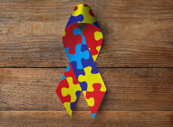 World Autism Awareness Day. Colorful puzzle ribbon on wooden background, top view