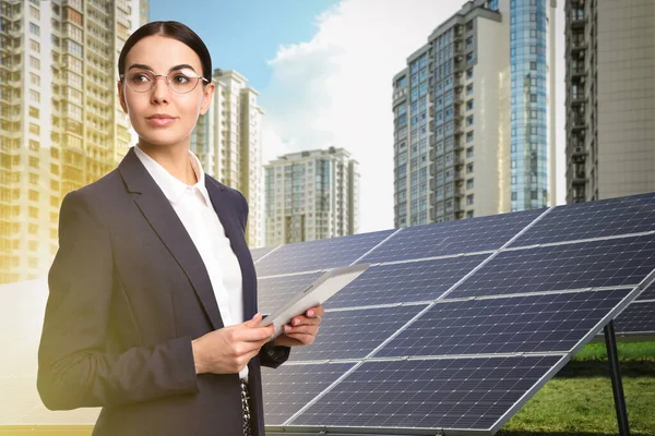 Young businesswoman with tablet near solar panels and beautiful view of cityscape. Alternative energy source