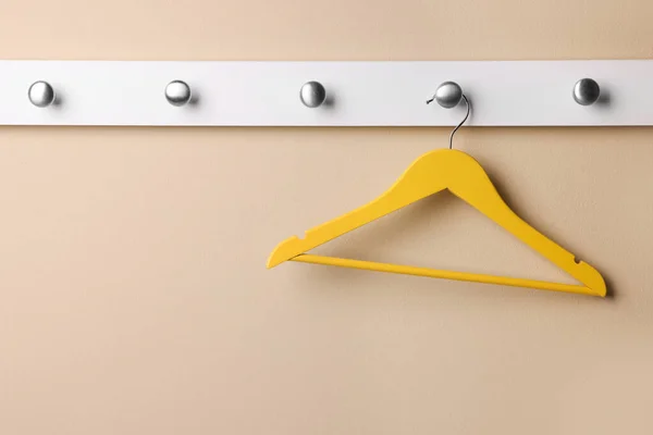 Rack with empty yellow clothes hanger on beige wall