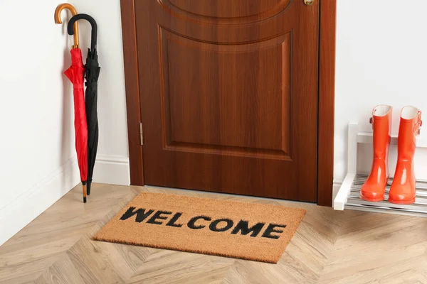 Door mat with word Welcome on wooden floor in hall