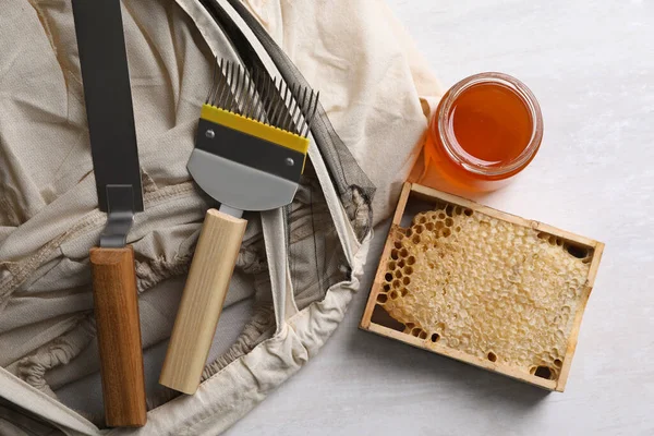 Different beekeeping tools and jar of honey on white table, flat lay