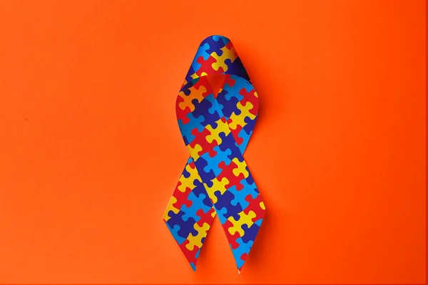 世界自閉症の日 オレンジ色の背景にカラフルなパズルリボン トップビュー — ストック写真