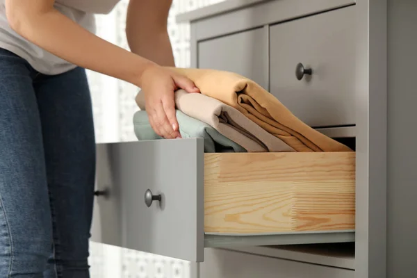 Woman putting clean clothes into drawer at home, closeup