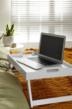 Beyaz tepsi ve yatağın içinde modern laptop var.