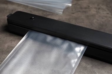 Gri masa üzerinde plastik torba ile vakum paketi için mühür, yakın plan.