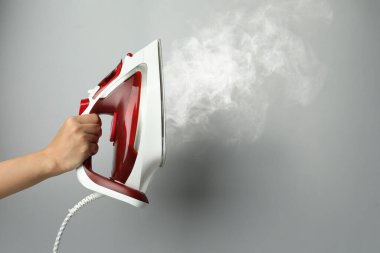 Açık gri arka planda buharlı modern demiri tutan kadın, yakın plan. Metin için boşluk