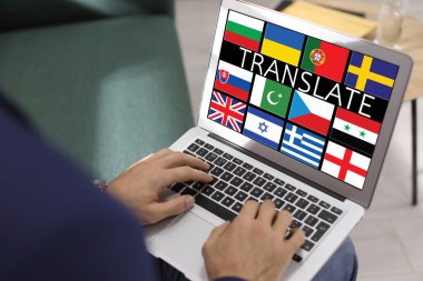 Translator using modern laptop with images of different flags on screen in office, closeup