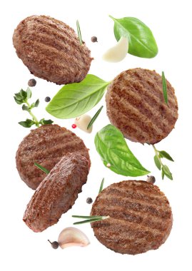 Beyaz arka plana dökülen lezzetli ızgara hamburger köfteleri ve baharatlar.