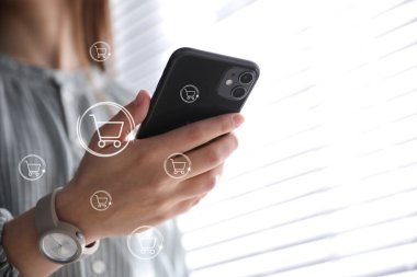 Teslimat konsepti. Modern cep telefonunu kapalı mekanlarda alışveriş yapmak için kullanan bir kadın. Pazar arabası çizimleri