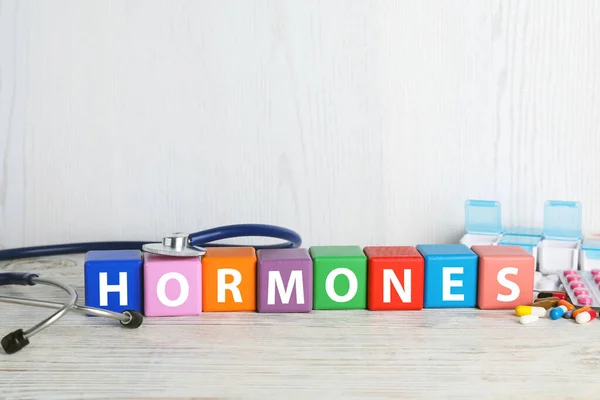 单词Hormones由五彩缤纷的立方体 听诊器和白色木制桌子上的药丸制成 — 图库照片