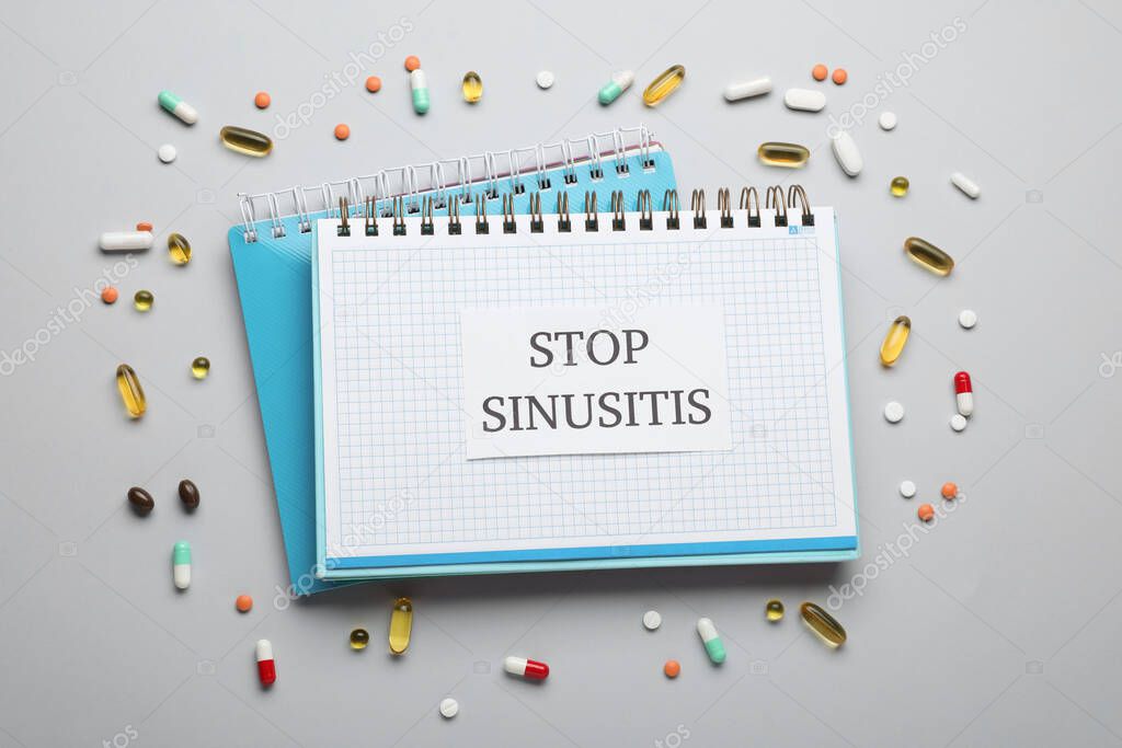 Notebook with word SINUSITIS surrounded by different pills on grey background, flat lay