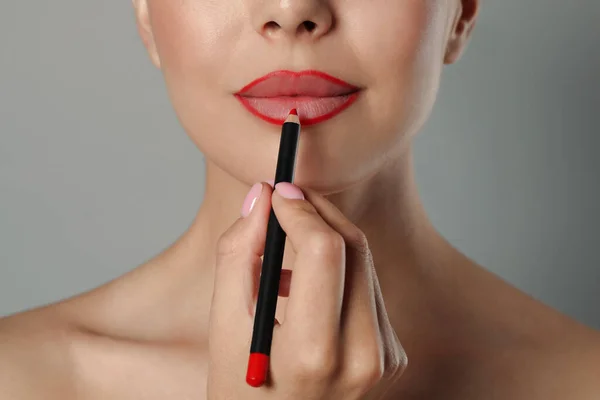 Jonge Vrouw Aanbrengen Mooie Rode Lip Potlood Grijze Achtergrond Close — Stockfoto