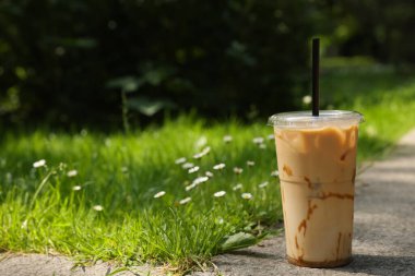 Dışarıdaki yeşil çimlerin yanında soğuk kahve bardağı ve pipetle servis edilen plastik bardaklar.