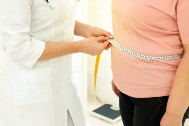 Klinikte kilolu kadının belini bantla ölçen beslenme uzmanı.