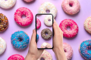 Kadın menekşe arka planda lezzetli donutların fotoğrafını çekiyor.