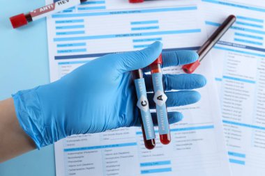 Scientist holding tubes with blood samples for hepatitis virus test near laboratory form, closeup
