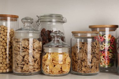 Rafta farklı kahvaltı gevrekleri olan cam kaplar.