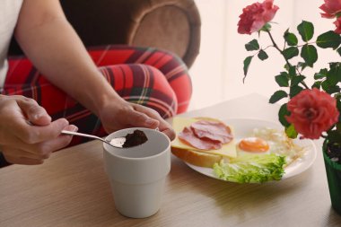 Sabah kahvesini hazırlayan kadın içeride, ahşap masada kahvaltı ederken, yakın plan.