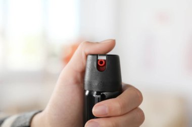 Woman using pepper spray on blurred background, closeup