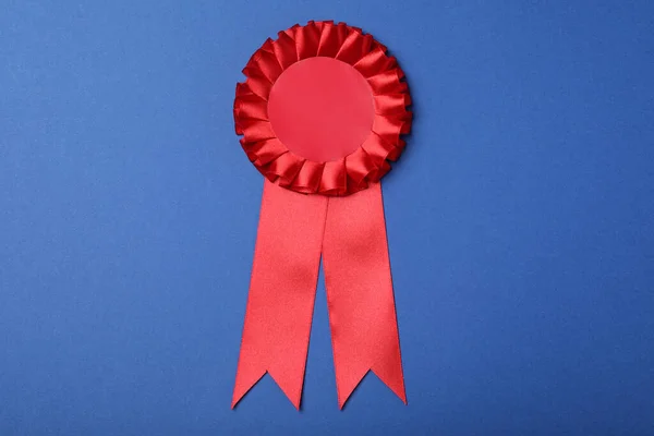 Red award ribbon on blue background, top view