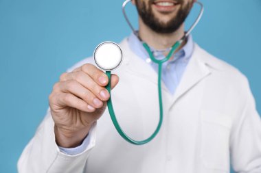 Açık mavi arka planda steteskobu olan doktor, yakın plan. Kardiyoloji kavramı