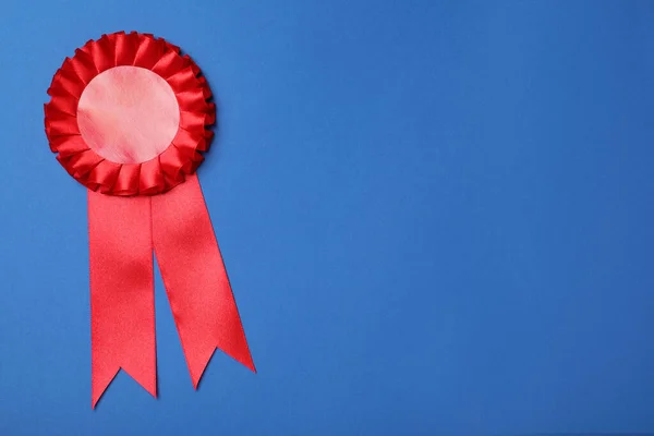 Red award ribbon on blue background, top view. Space for text