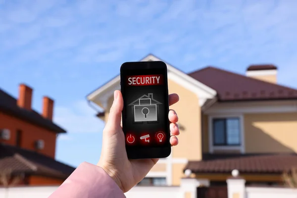 Woman using home security app on smartphone outdoors, closeup