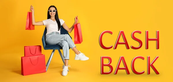 Beautiful woman with paper shopping bags in armchair and words Cash Back on yellow background. Banner design