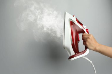 Açık gri arka planda buharlı modern demiri tutan kadın, yakın plan. Metin için boşluk