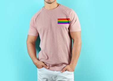 Young man wearing pink t-shirt with image of LGBT pride flag on turquoise background