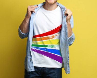 Sarı arka planda LGBT gurur bayrağı resmi olan beyaz tişört giyen genç adam