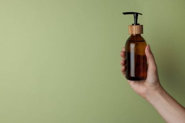 Kadının elinde soluk zeytinli arka planda kozmetik ürünü şişesi var. Yakın plan. Metin için boşluk