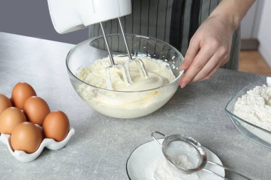 Woman whipping white cream with mixer at light grey table, closeup clipart