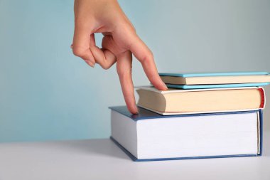 Woman imitating stepping up on books with her fingers against light blue background, closeup