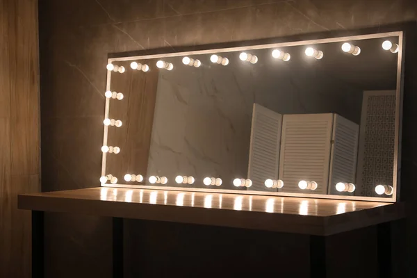Modern mirror with light bulbs on wooden table in room