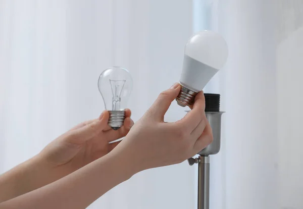 Woman changing incandescent light bulb for fluorescent one in lamp at home, closeup. Saving energy concept